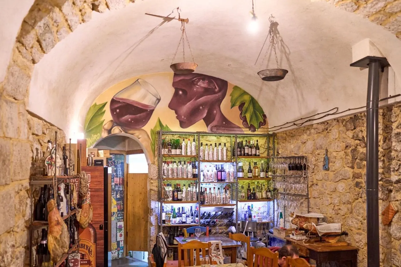 La sala dell'enoteca: volta in pietra, murale con calice di vino e scaffali di bottiglie